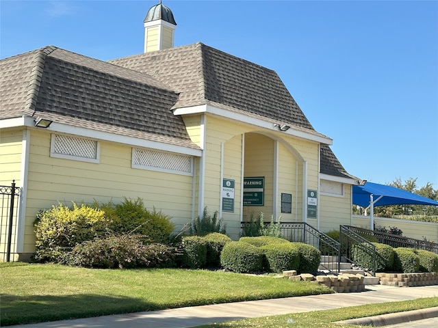 view of front of home with a shingled roof, a front lawn, and mansard roof