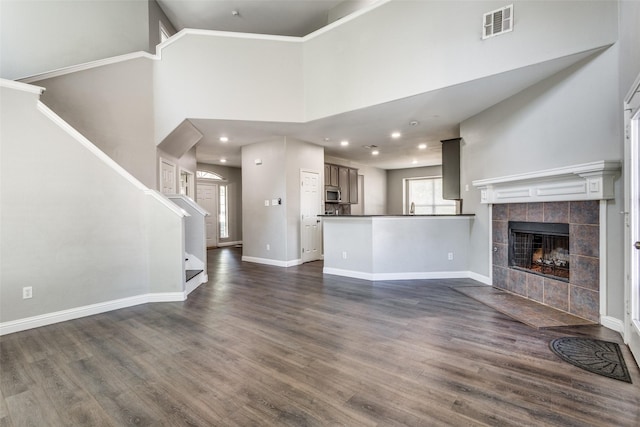 unfurnished living room featuring dark wood-style flooring, visible vents, a high ceiling, a tile fireplace, and baseboards