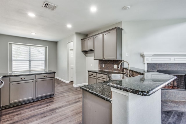 kitchen featuring a peninsula, wood finished floors, a sink, visible vents, and decorative backsplash