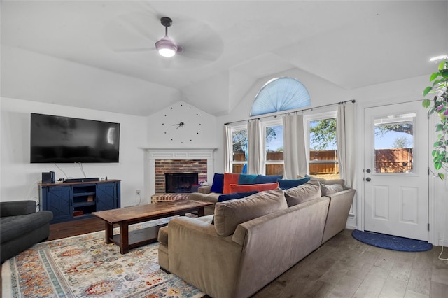 living room with a brick fireplace, a ceiling fan, vaulted ceiling, and wood finished floors