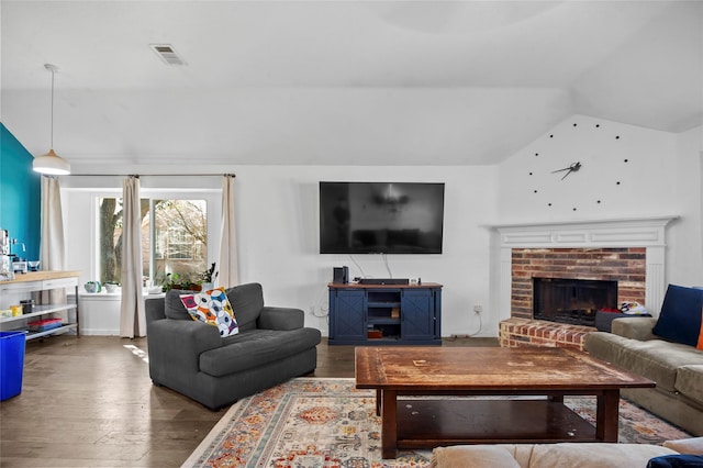 living area featuring vaulted ceiling, a fireplace, wood finished floors, and visible vents