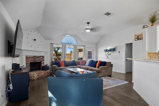 living area with a ceiling fan, a brick fireplace, vaulted ceiling, and dark wood-style floors