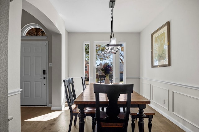 dining room with a wainscoted wall, dark wood-type flooring, and a decorative wall