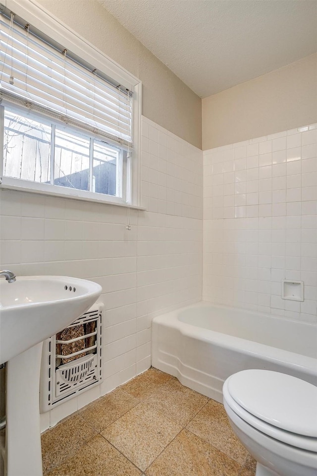 bathroom featuring a textured ceiling, toilet, a sink, tile walls, and a bathtub