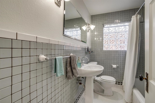 bathroom featuring tile walls, toilet, shower / tub combo with curtain, tile patterned floors, and a sink