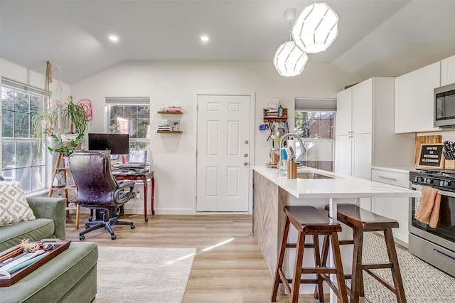 kitchen with lofted ceiling, a sink, white cabinetry, light countertops, and appliances with stainless steel finishes