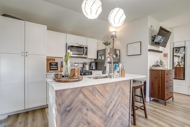 kitchen featuring light wood-type flooring, white cabinetry, stainless steel appliances, and a sink