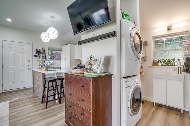 laundry room with light wood-style floors, laundry area, a sink, and stacked washing maching and dryer