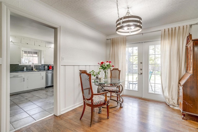 dining area featuring french doors, a wainscoted wall, crown molding, and light wood-style flooring