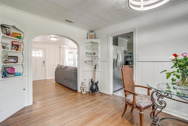 interior space featuring arched walkways, a decorative wall, visible vents, light wood finished floors, and crown molding