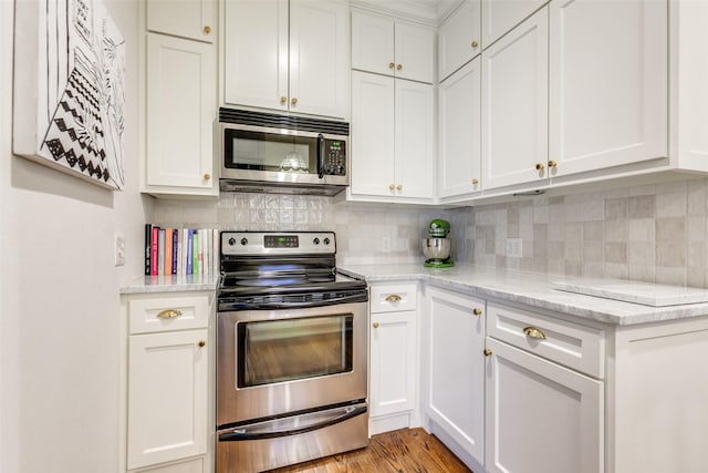 kitchen with tasteful backsplash, appliances with stainless steel finishes, white cabinets, and light wood-style flooring