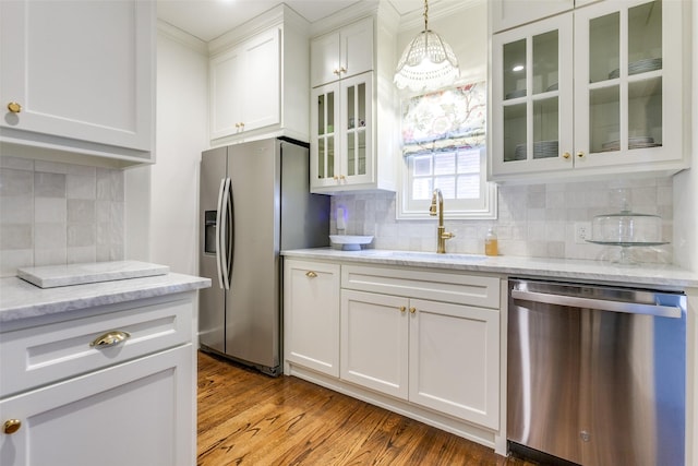 kitchen with wood finished floors, a sink, white cabinets, appliances with stainless steel finishes, and light stone countertops