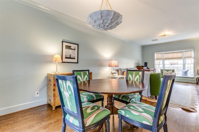 dining space featuring baseboards, wood finished floors, visible vents, and crown molding