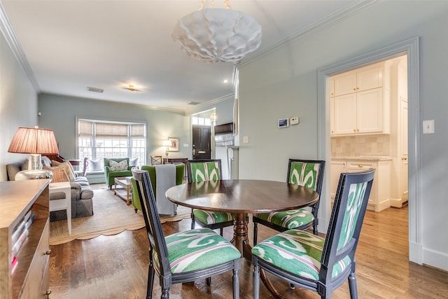 dining area featuring light wood-style floors, visible vents, and ornamental molding