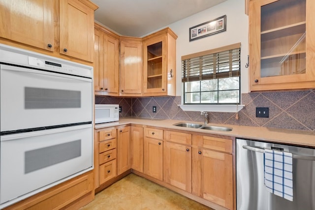 kitchen with light brown cabinets, white appliances, a sink, decorative backsplash, and glass insert cabinets