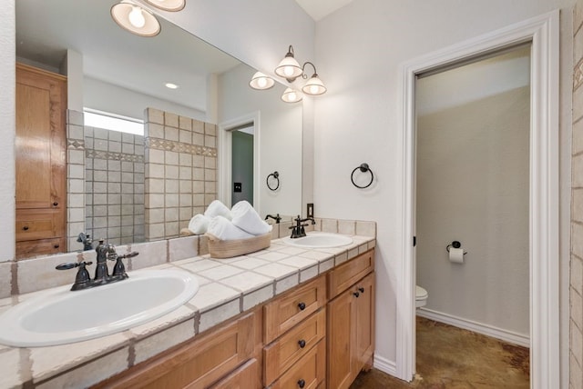 full bath featuring double vanity, a sink, toilet, and baseboards