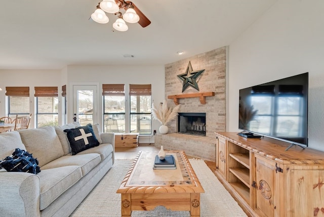 living area with a large fireplace, ceiling fan, and visible vents