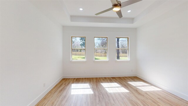 spare room featuring a tray ceiling, light wood-style flooring, baseboards, and recessed lighting