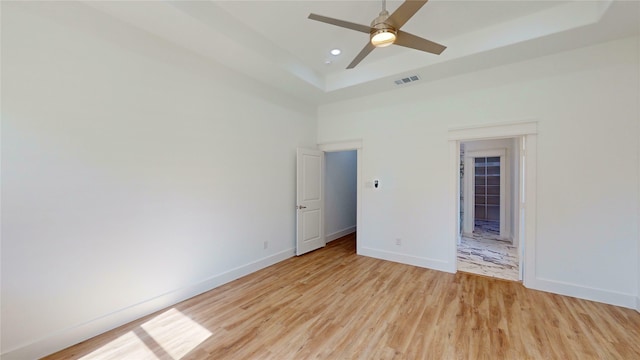 unfurnished bedroom with a tray ceiling, visible vents, light wood-style flooring, and baseboards