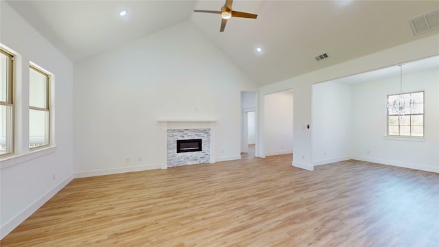 unfurnished living room with ceiling fan with notable chandelier, light wood finished floors, a tiled fireplace, and visible vents