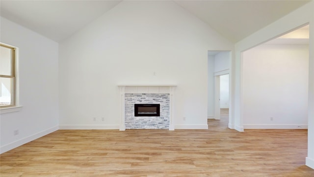 unfurnished living room featuring high vaulted ceiling, a tile fireplace, light wood-style flooring, and baseboards