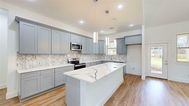 kitchen with gray cabinetry, appliances with stainless steel finishes, light wood-type flooring, light stone countertops, and tasteful backsplash