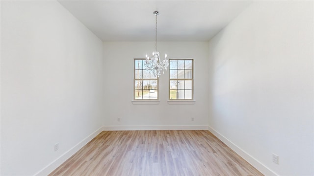 spare room with baseboards, light wood-type flooring, and an inviting chandelier