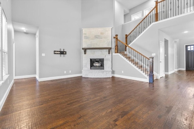 unfurnished living room featuring a high ceiling, stairway, baseboards, and wood finished floors