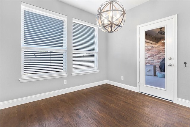 unfurnished dining area with a healthy amount of sunlight, dark wood-style flooring, an inviting chandelier, and baseboards