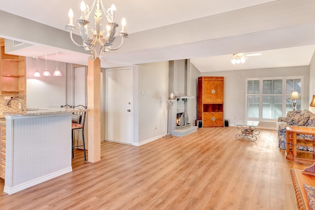 living room with ceiling fan, a brick fireplace, light wood-style flooring, and baseboards