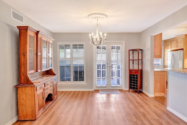 unfurnished dining area featuring baseboards, visible vents, an inviting chandelier, french doors, and light wood-style floors