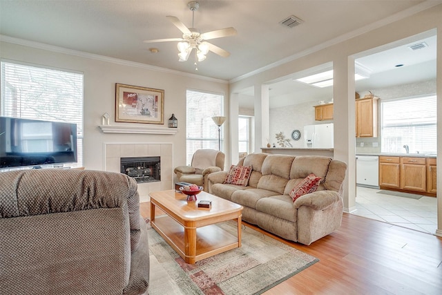 living room with light wood-type flooring, a tiled fireplace, visible vents, and crown molding