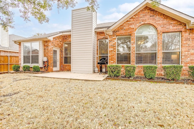 rear view of property featuring a patio area, brick siding, fence, and a chimney