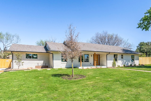 ranch-style home with brick siding, fence, a front lawn, and roof with shingles