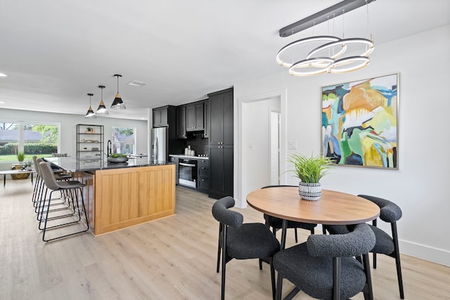 kitchen featuring dark cabinets, visible vents, stainless steel fridge with ice dispenser, light wood finished floors, and an island with sink