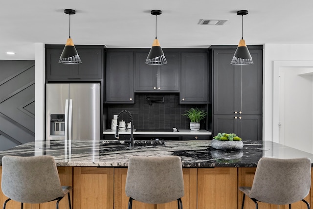 kitchen featuring a breakfast bar, stainless steel fridge, decorative backsplash, and dark stone countertops