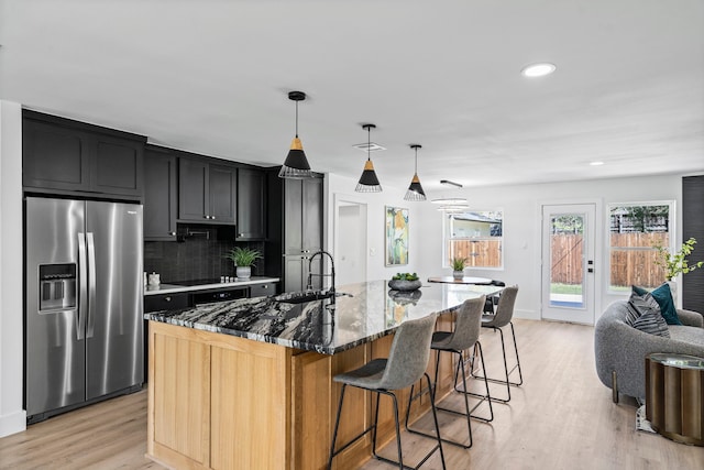 kitchen featuring dark cabinets, a sink, dark stone counters, light wood finished floors, and stainless steel fridge