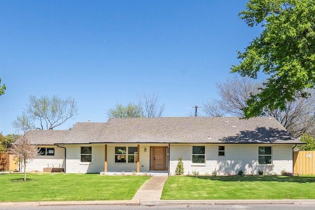 ranch-style house featuring a shingled roof, a front yard, fence, and brick siding