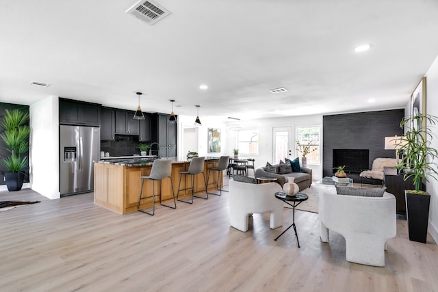 living room with light wood-type flooring, a large fireplace, and visible vents