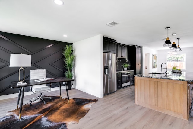 kitchen featuring light stone counters, stainless steel refrigerator with ice dispenser, a sink, dark cabinets, and light wood-type flooring