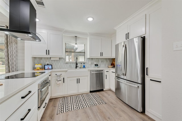 kitchen with island range hood, appliances with stainless steel finishes, light countertops, light wood-style floors, and a sink