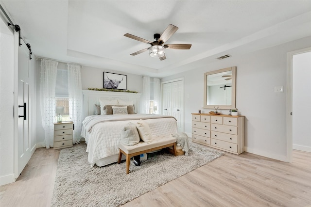 bedroom featuring a barn door, visible vents, baseboards, a tray ceiling, and light wood-style floors