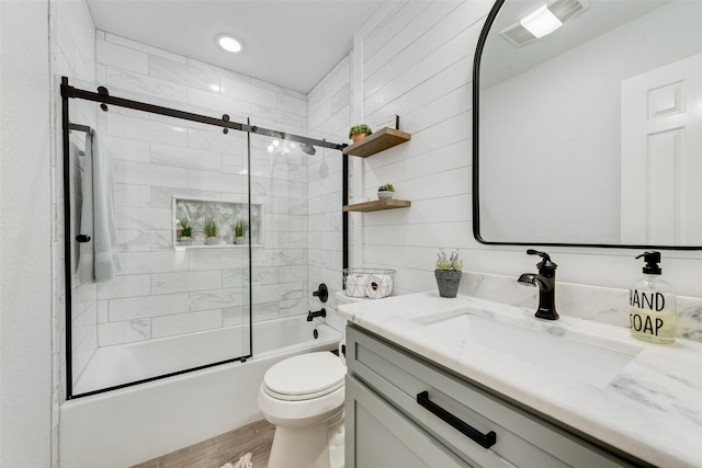 bathroom with shower / bath combination with glass door, visible vents, toilet, vanity, and wood finished floors