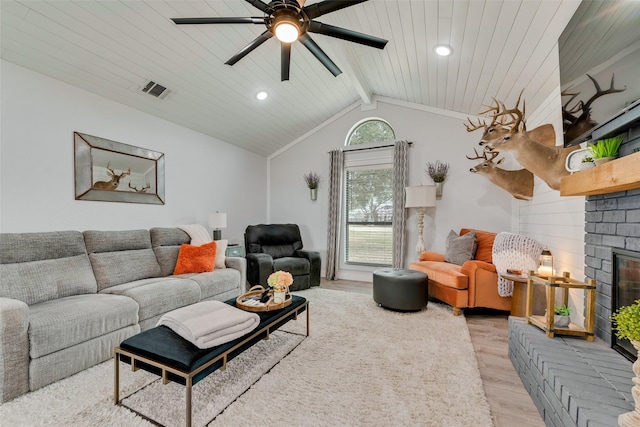 living room featuring vaulted ceiling with beams, visible vents, light wood-style floors, a ceiling fan, and a brick fireplace