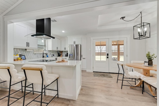 kitchen featuring a peninsula, a kitchen breakfast bar, light countertops, stainless steel refrigerator with ice dispenser, and island exhaust hood