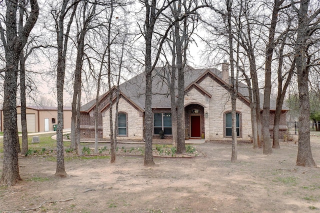 view of front facade featuring stone siding, a shingled roof, a chimney, and brick siding