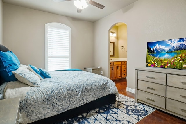 bedroom with arched walkways, ensuite bath, a ceiling fan, and baseboards