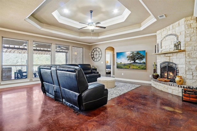 living area with visible vents, a raised ceiling, arched walkways, and a stone fireplace