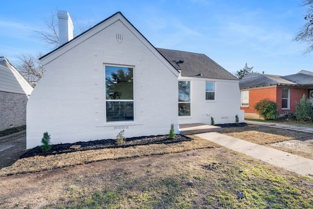 exterior space with crawl space, roof with shingles, a chimney, and brick siding