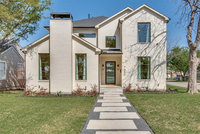 view of front facade featuring a standing seam roof, a front lawn, a chimney, and brick siding